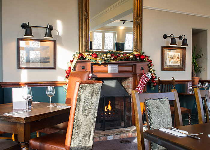 The interior of a pub, decorated for Christmas. Christmas baubles and a stocking is hanging over a lit fireplace
