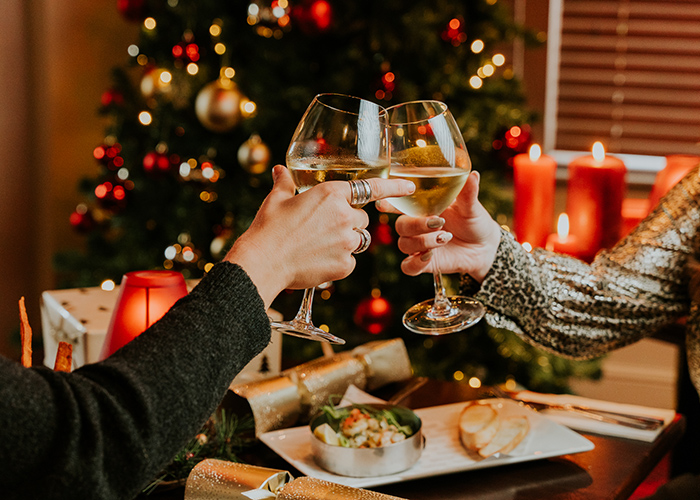 Two glasses being clinked together to “cheers!”  with seasonal dishes and decorations in the background